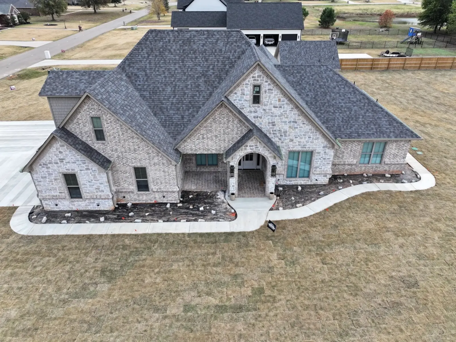 Aerial view of a finished stone home with a new charcoal architectural shingle roof by Bohon Roofing